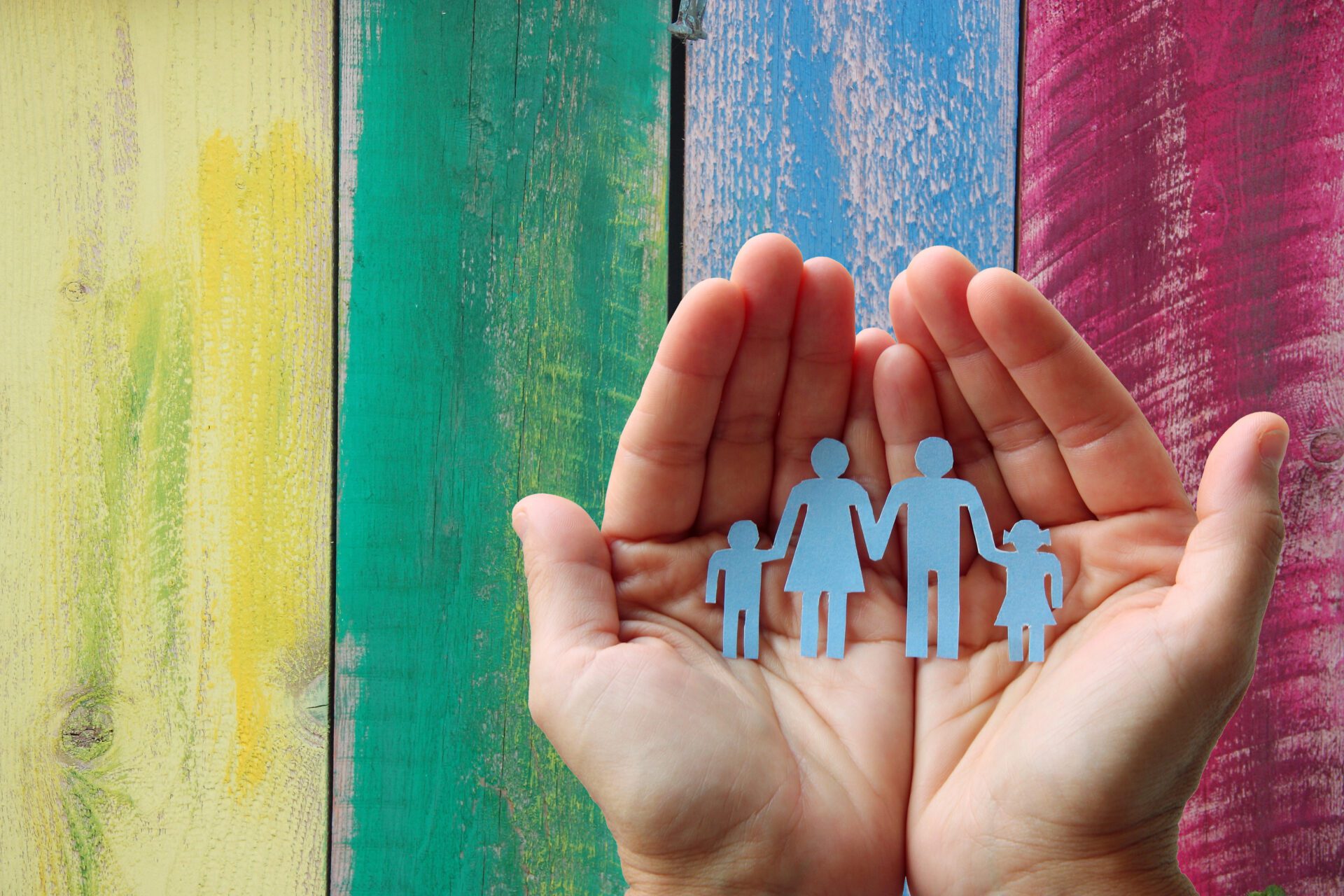 Image of a paper family in hands on wooden coloured background