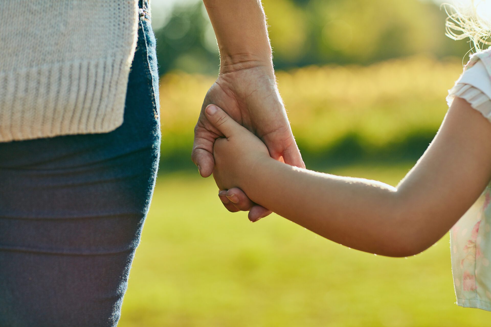 Image of a little girl holding an unrecognizable woman’s hand in the park